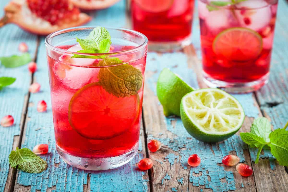 Club soda and cranberry juice in glasses with ice and slice of lime with fresh mint leaves on blue table.