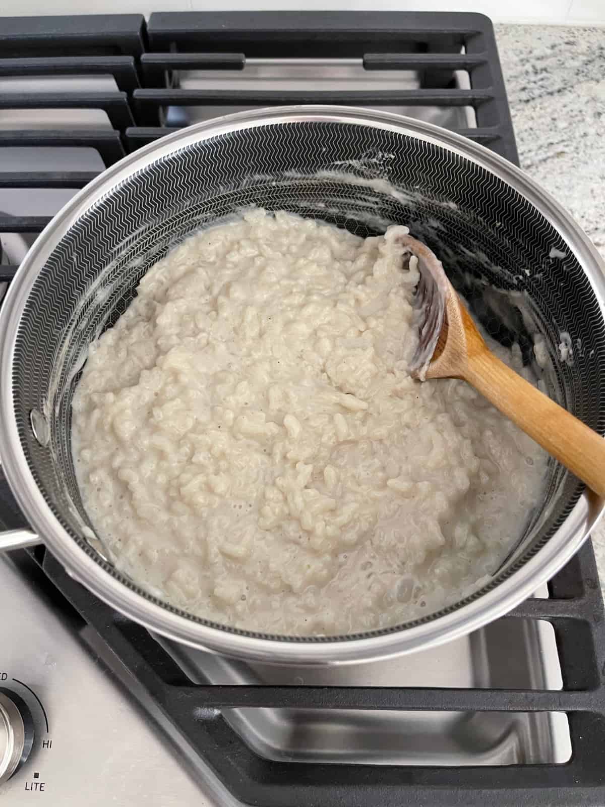 Cooking Arborio rice in milk with sugar and cardamom in saucepan on stovetop.