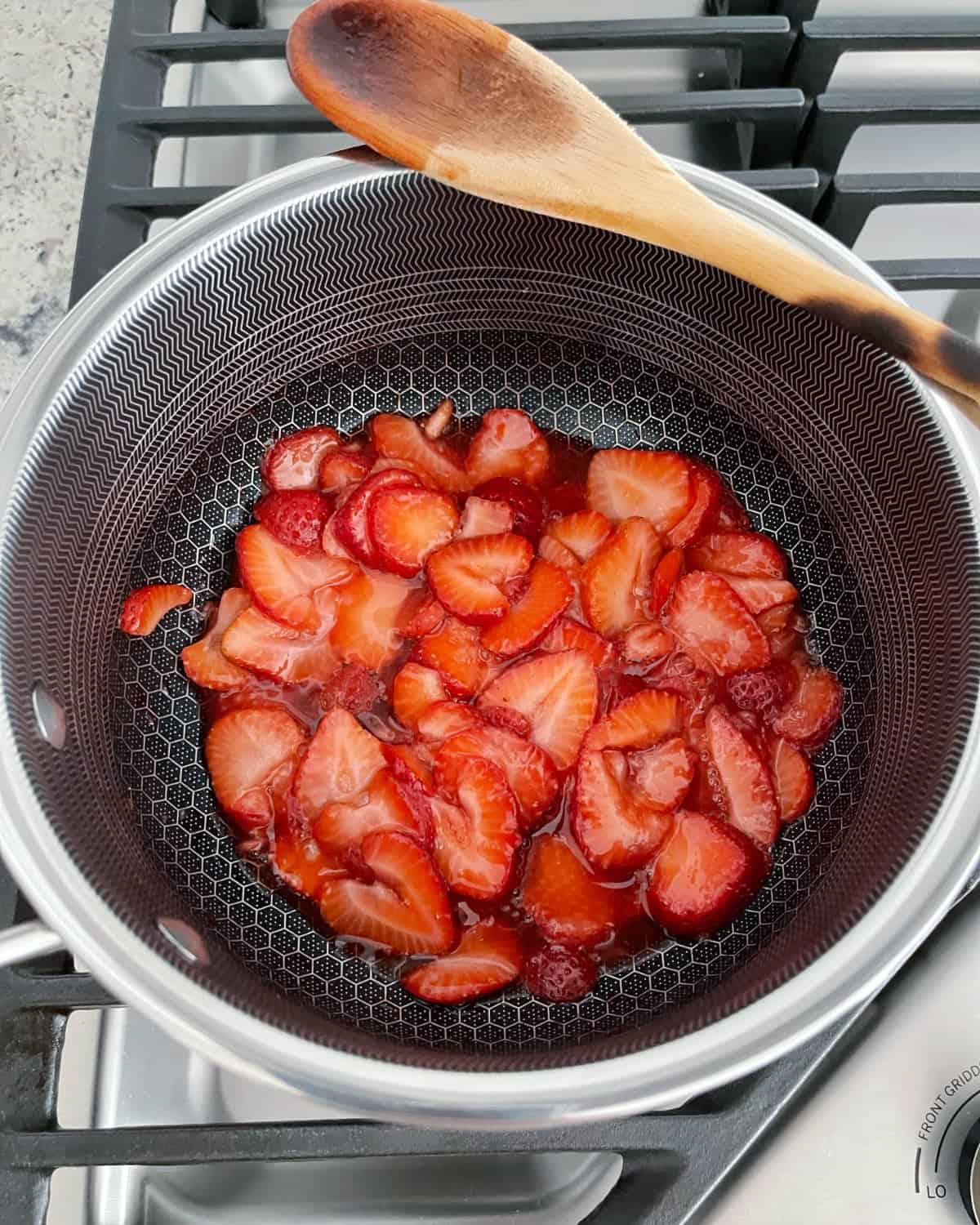 Heating sliced strawberries and sugar in saucepan on stovetop.