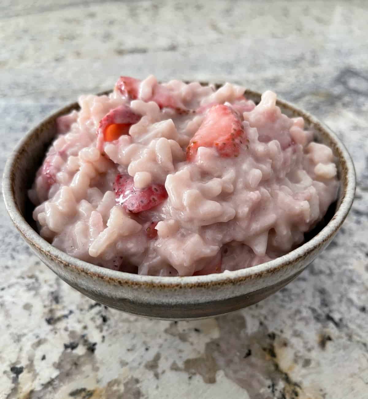 Skinny strawberry rice pudding in brown ceramic bowl on granite counter.