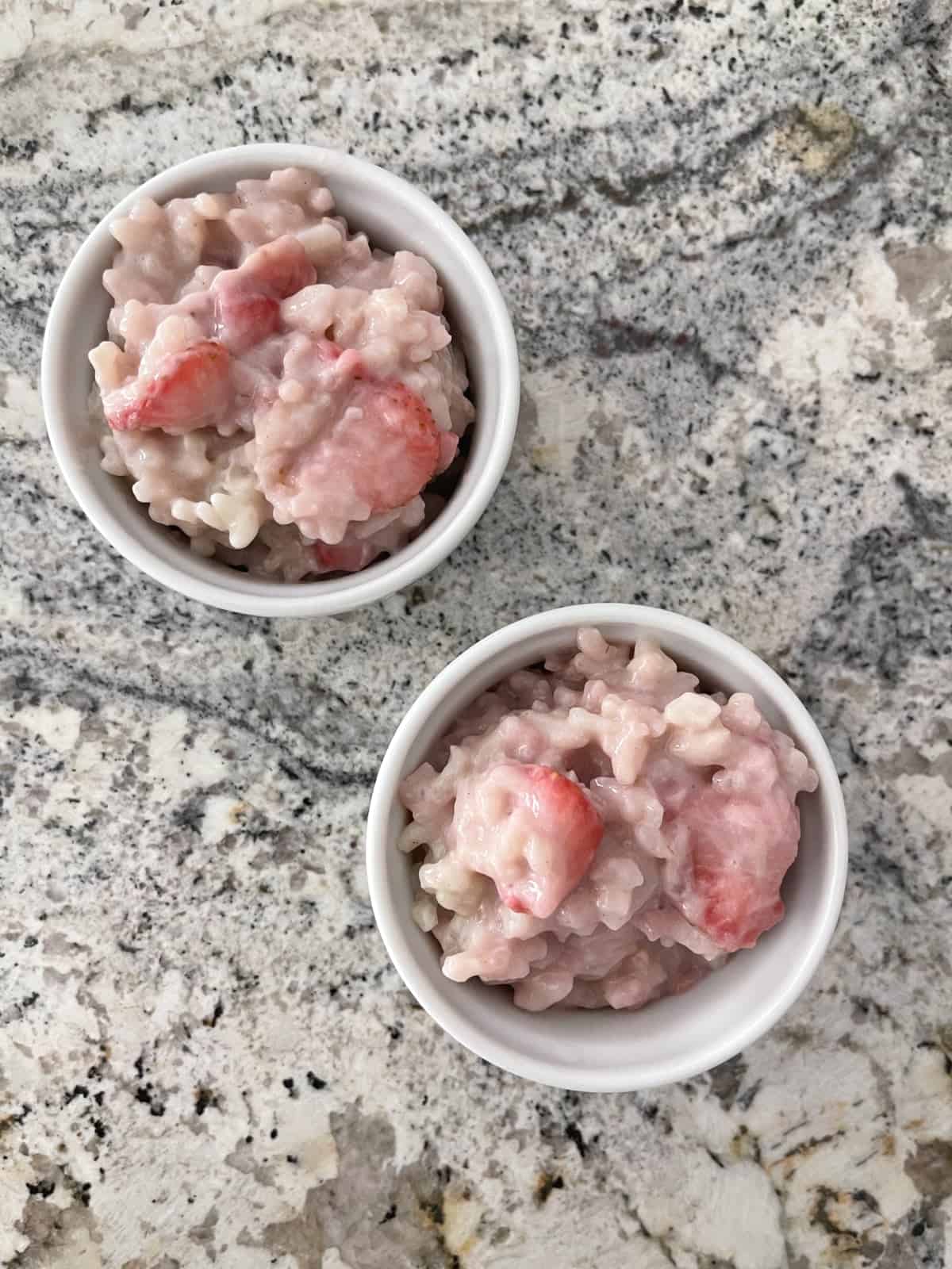 Strawberry rice pudding in two small white ramekins on granite.