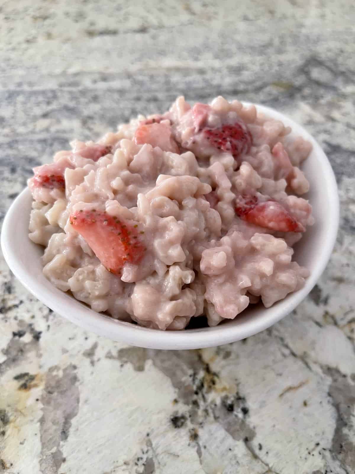 Creamy strawberry rice pudding in small white bowl on granite counter.