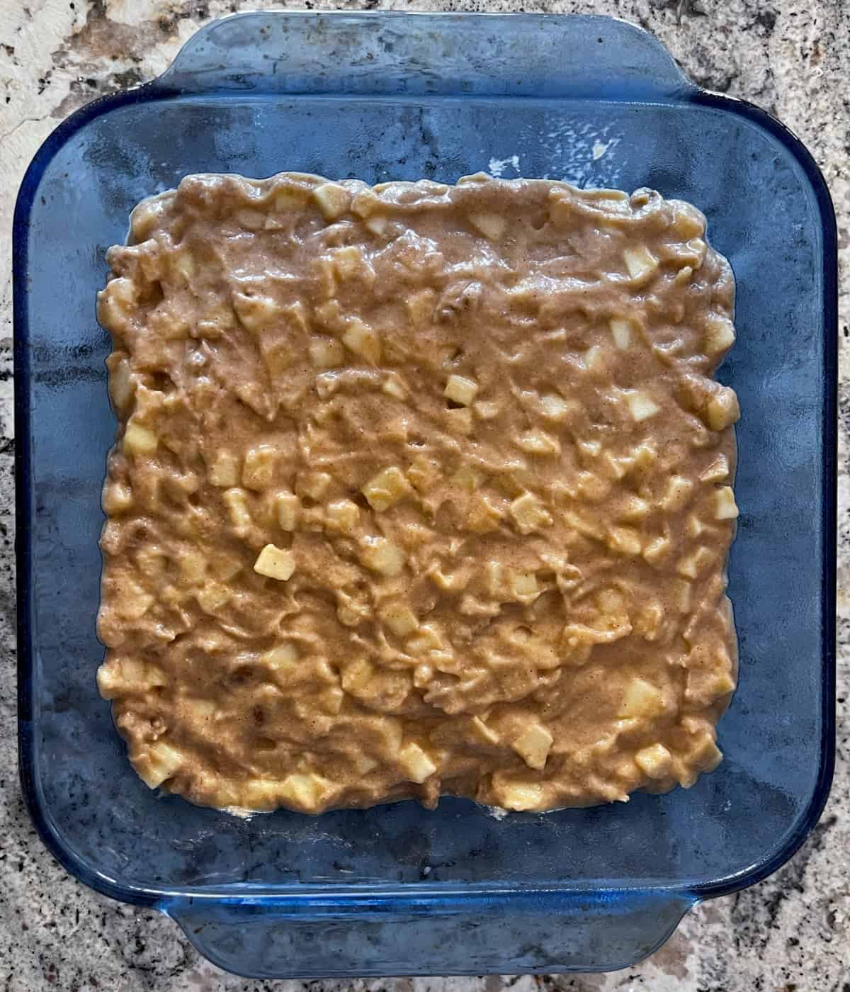 Blue baking dish filled with unbaked apple brownie nut bar batter.