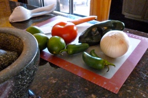 Fresh salsa ingredients including tomato, jalapeño, onion and lime on cutting mat.