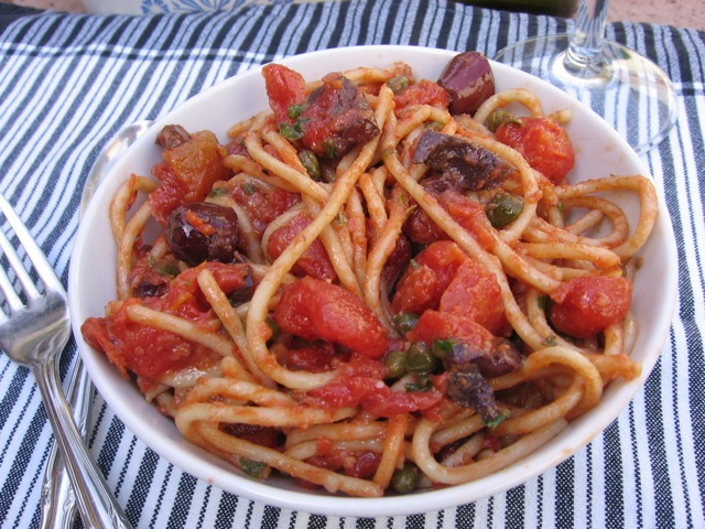 Spaghetti Puttanesca made gluten-free in white bowl with fork.