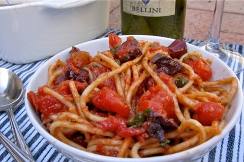 Gluten Free Pasta All Puttanesca in white bowl with spoon and bottle of wine.