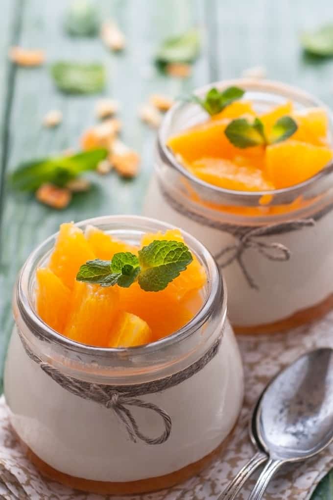 Jars of Orange Honey Panna Cotta with a spoon and fresh mint sprigs in small glasses with twine bows.