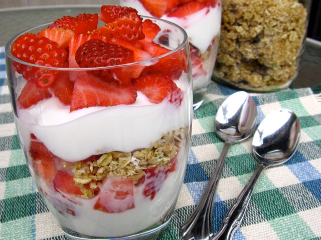 Strawberry, yogurt and granola parfaits in clear glasses on checked tablecloth