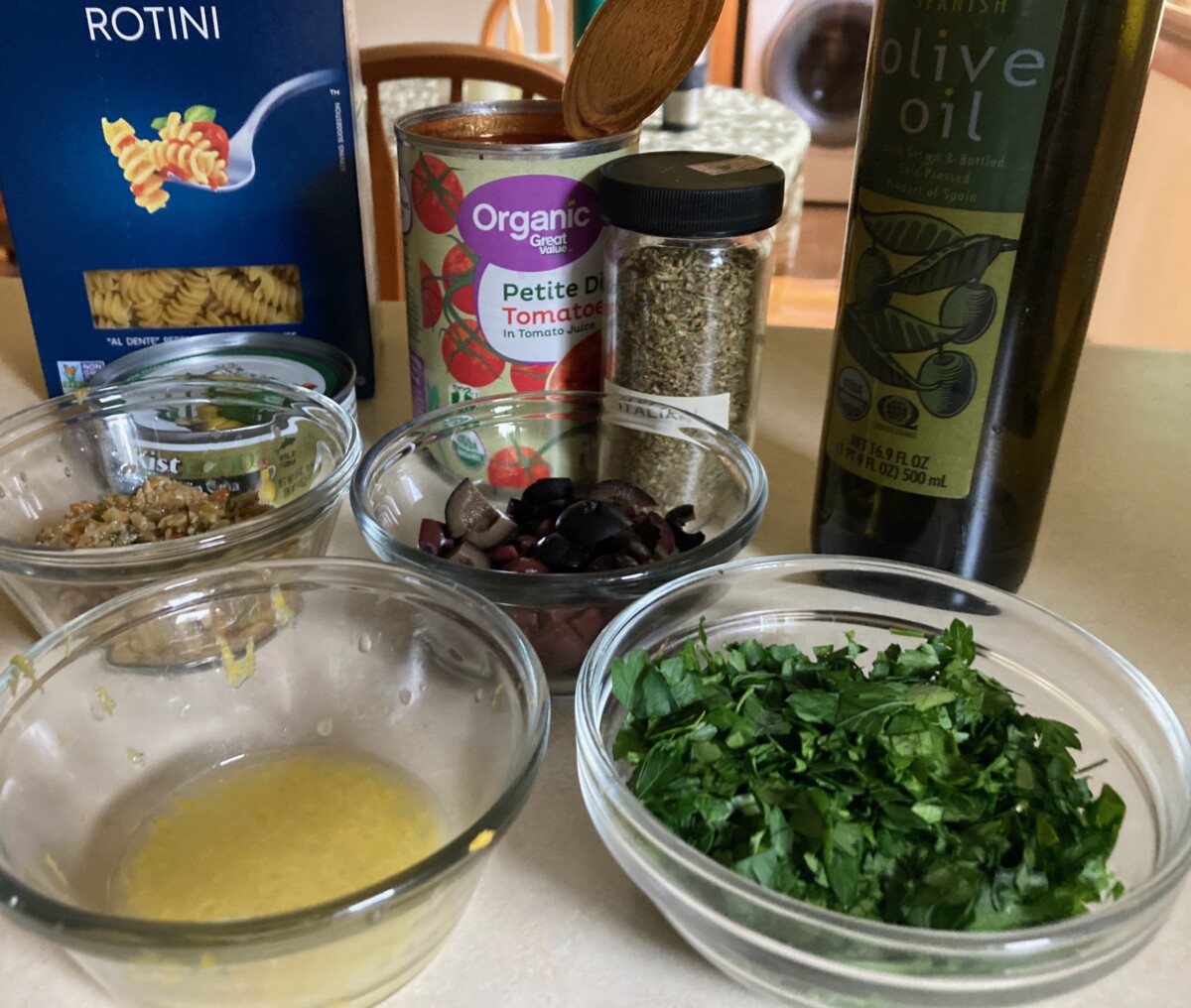 Ingredients including rotini pasta, olive oil, canned diced tomatoes, canned tuna, olives, capers, lemon juice and zest and parsley.