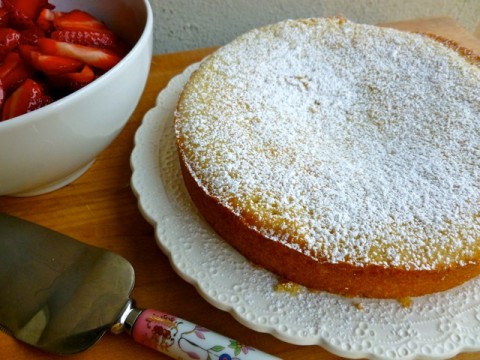 Skinny Vanilla Buttermilk Cake topped with powdered sugar near bowl of strawberries.