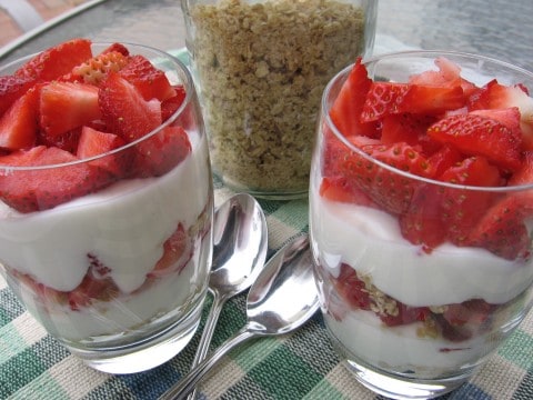 Two Strawberry Yogurt Granola Parfaits in glasses with spoons and a jar of granola