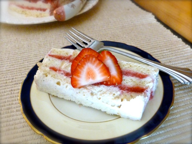 Light Frozen Strawberry Layer Cake slice topped with strawberry slices on plate with fork.