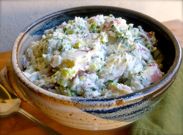 Creamy red potato salad in ceramic bowl with serving spoon.