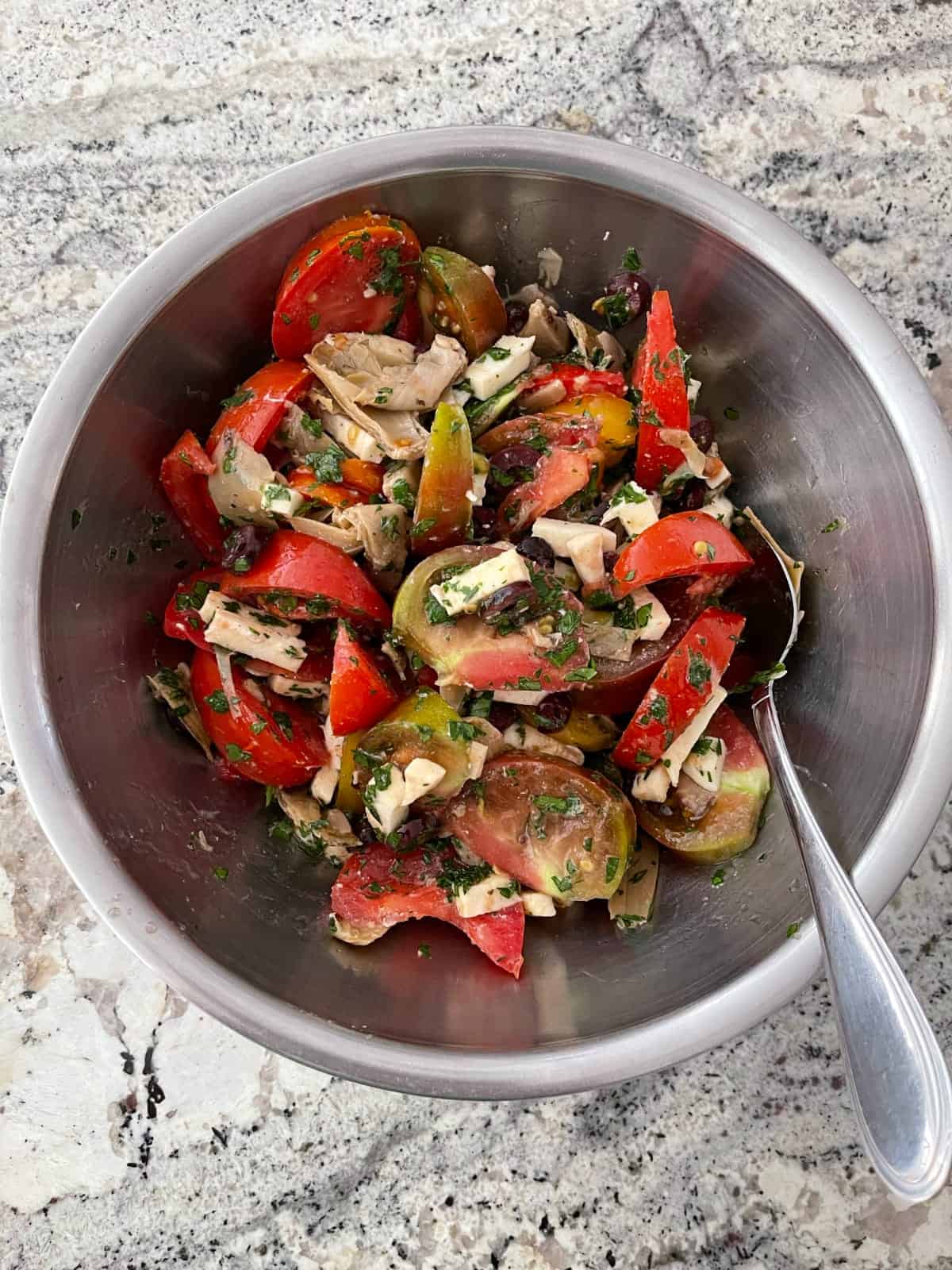 Tossing artichoke tomato salad in mixing bowl.