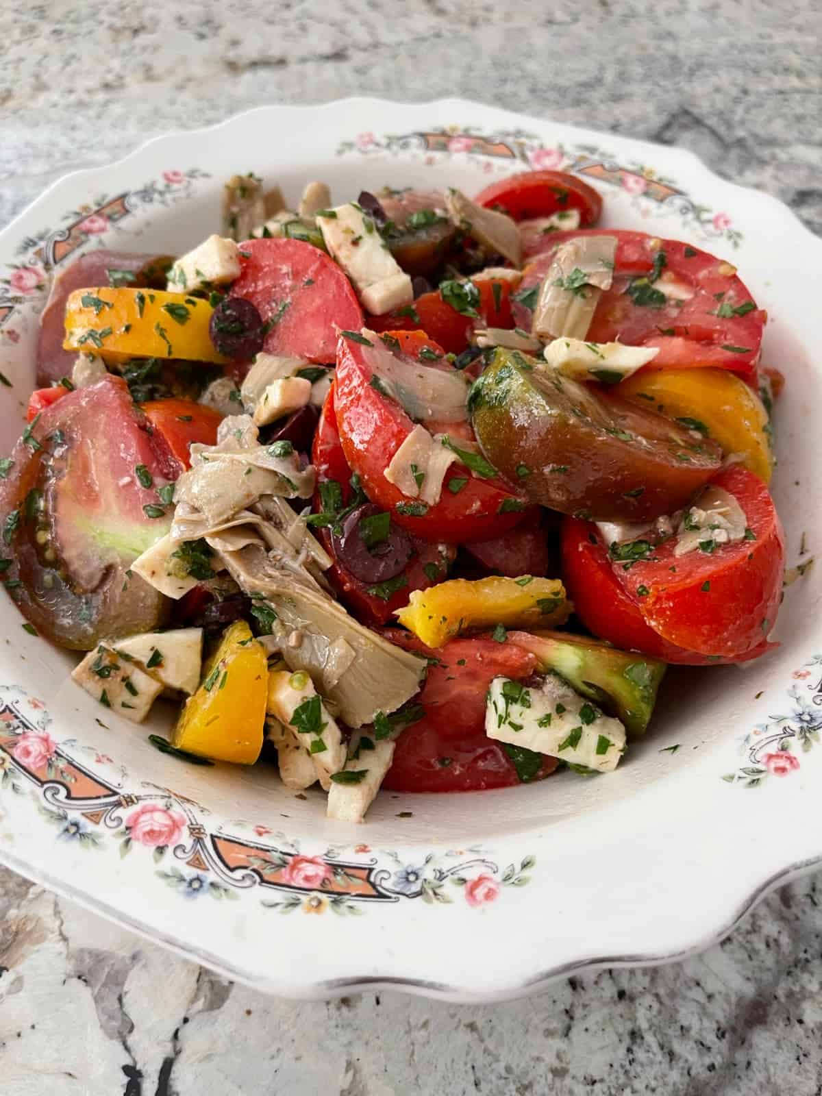Fresh tomato salad with artichokes, mozzarella and olives in serving bowl.