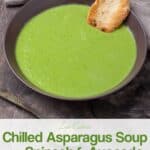 Chilled asparagus soup with crusty bread in dark bowl on wood table.