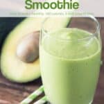 Creamy avocado pear smoothie in tall glass on wood table with two straws and avocado cut in half