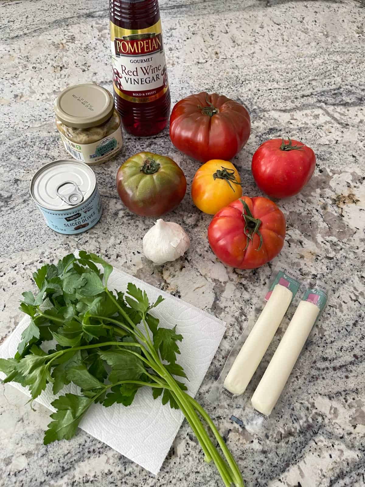 Ingredients including red wine vinegar, fresh tomatoes, olives, artichoke quarters, parsley, string cheese and garlic.