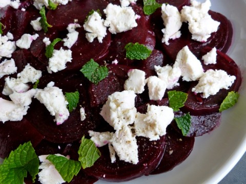 Marinated Roasted Beet Salad topped with goat cheese and fresh mint leaves on white plate.
