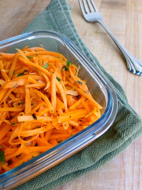 Square glass container of shredded French carrot salad on a green napkin.