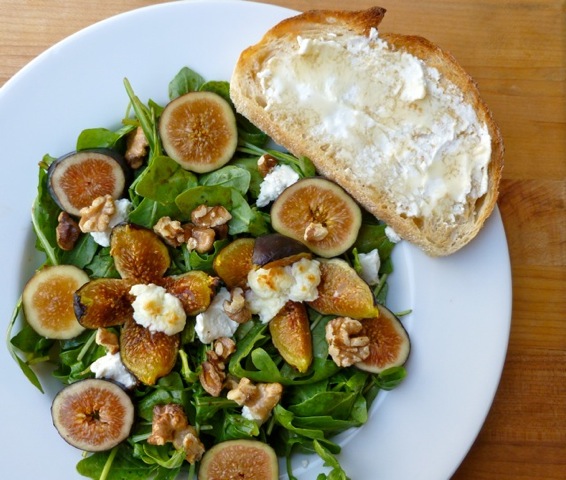Warm Fig and Goat Cheese Salad on white plate with slice of bread and butter.