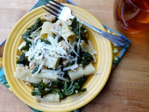 Pasta with chicken sausage and kale and shredded Parmesan on yellow dinner plate with fork.