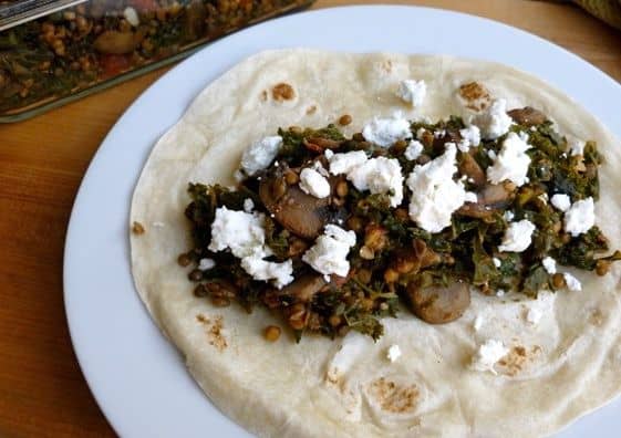 Filling tortilla with lentil, mushrooms and kale topped with crumbled goat cheese