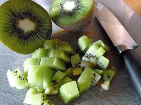 Chopping a fresh kiwi fruit with a knife on cutting board