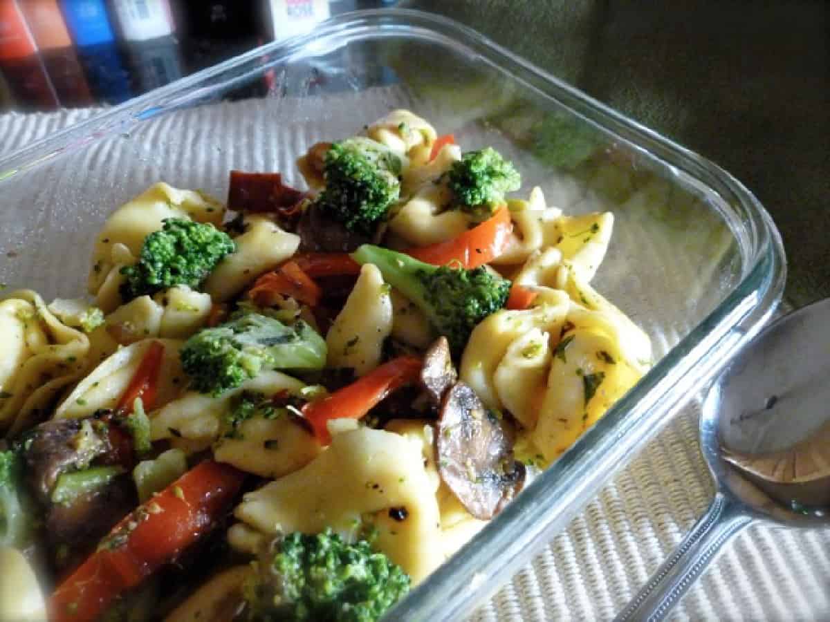 Cheese tortellini with mushrooms, broccoli and red peppers in small glass dish with spoon.