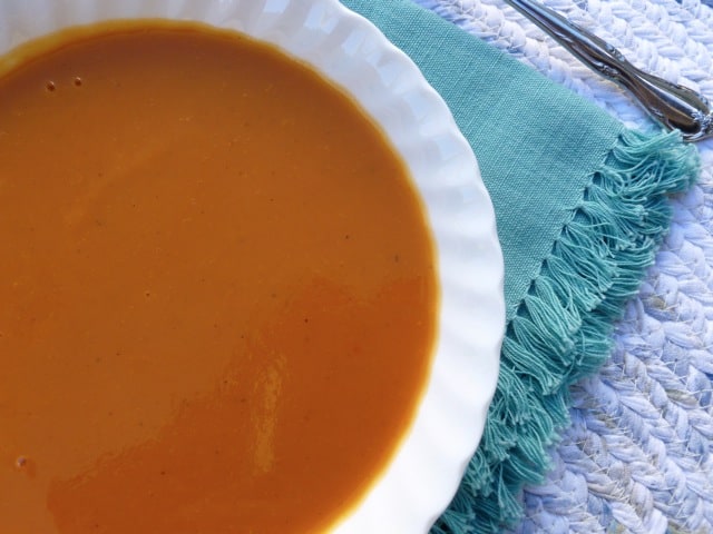 Sweet potato tomato soup in white bowl on blue mat.