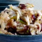 Mayo-free apple cole slaw with cranberries and walnuts in blue ceramic bowl.