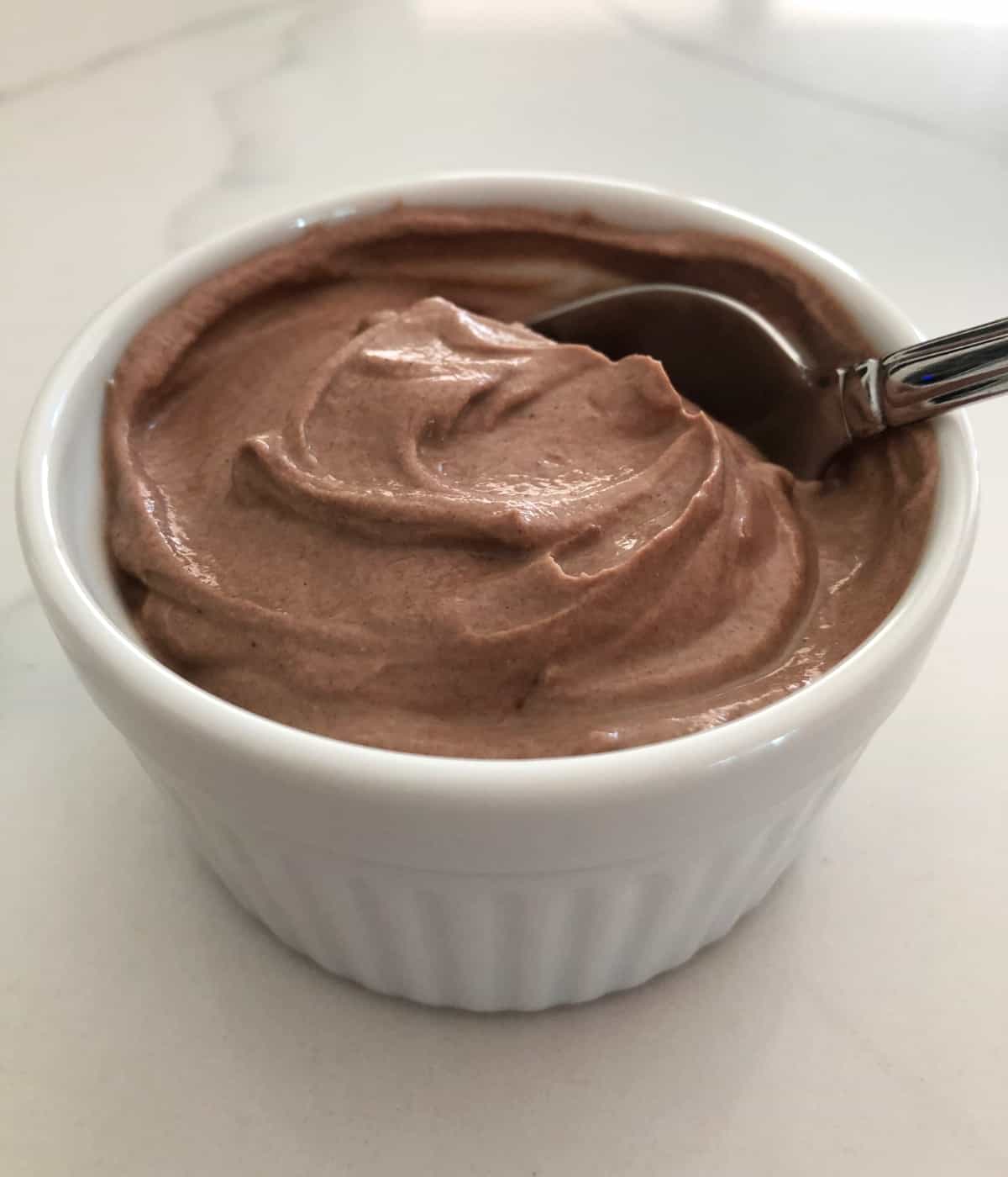 Creamy chocolate yogurt in white ramekin with spoon.