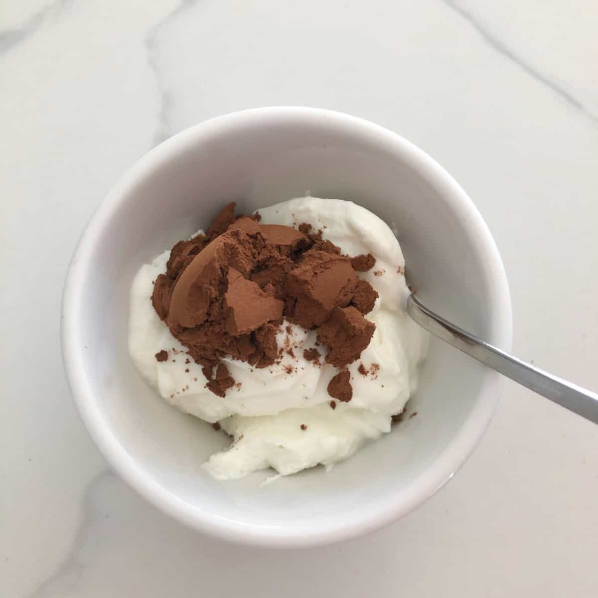 Nonfat Greek yogurt with cocoa powder in small white bowl with spoon.