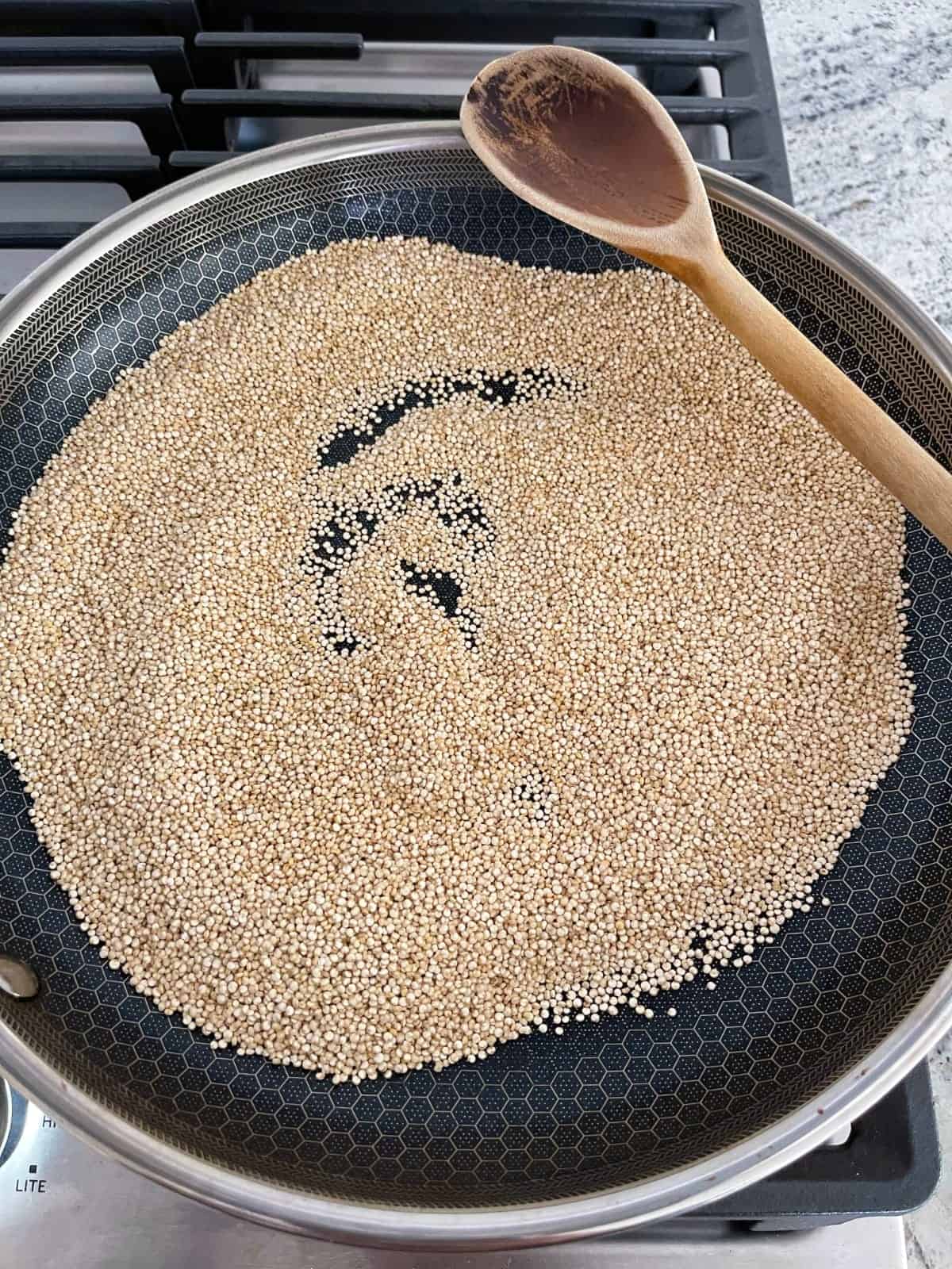 Toasting quinoa to golden brown in skillet on stovetop.