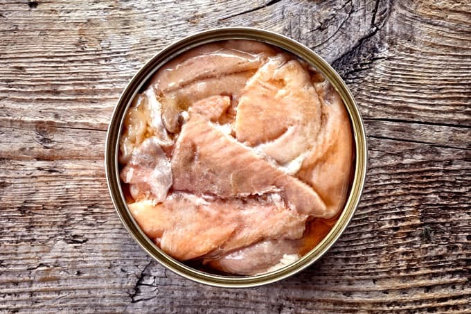 Open tin can, canned salmon, on wood table from above.