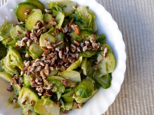 Brussles Sprouts Salad topped with toasted pecans in a white bowl
