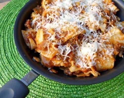 Lasagna in a Skillet with Noodles, Ground Beef, Tomato Sauce and Topped with Grated Cheese Sitting on a Green Woven Placemat