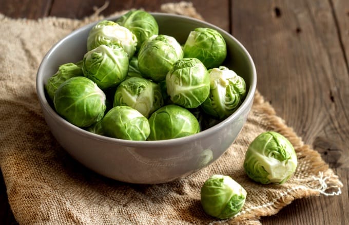 Fresh Brussels sprouts in a bowl on an old wooden table on a piece of burlap