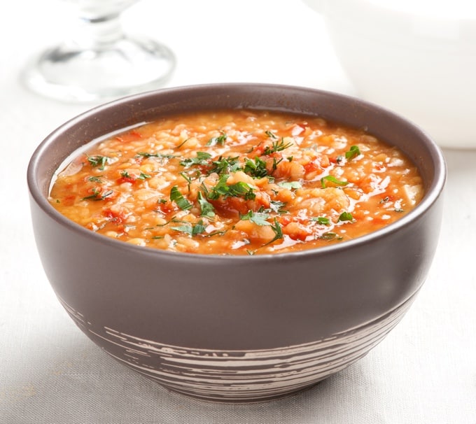 Lentil tabbouleh soup in brown bowl on white table.