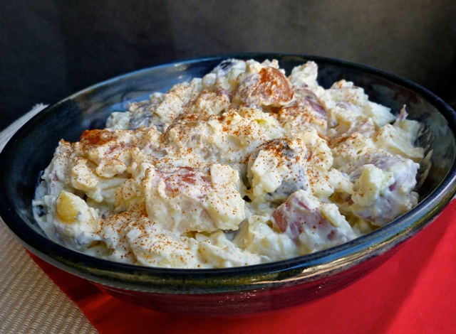 Creamy Red, White and Blue Potato Salad in blue bowl on red mat