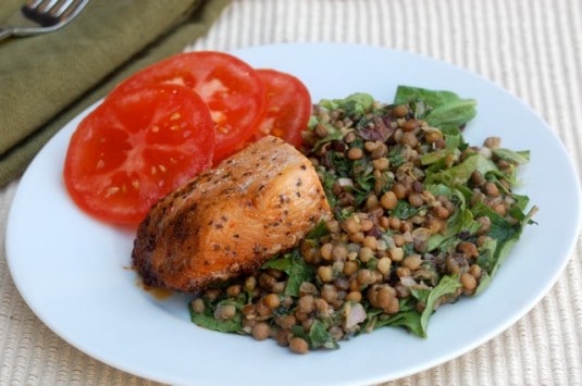 Salmon and Warm Lentil Salad with sliced tomatoes on white dinner plate.