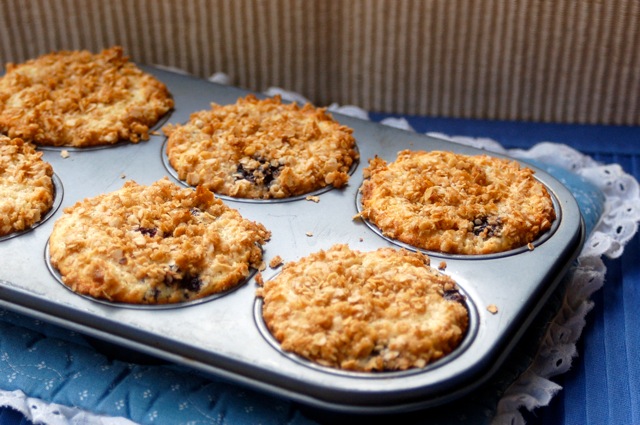 Blueberry muffins with streusel topping in a muffin tin on a blue and white pot holder.