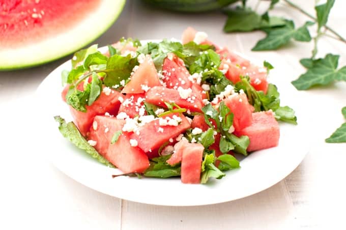 Watermelon crumbled feta salad on white plate with fresh watermelon in background.