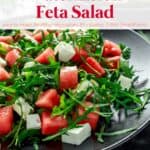 Watermelon feta salad with arugula on black plate with fresh watermelon slices in background.