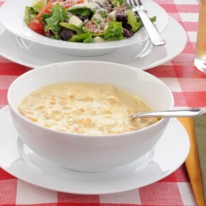 Bowl of corn chowder with a mixed green salad on a table with a red checkered table cloth