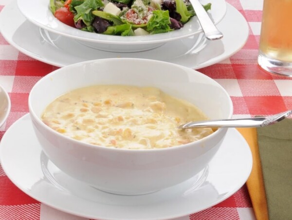 Bowl of corn chowder with a mixed green salad on a table with a red checkered table cloth