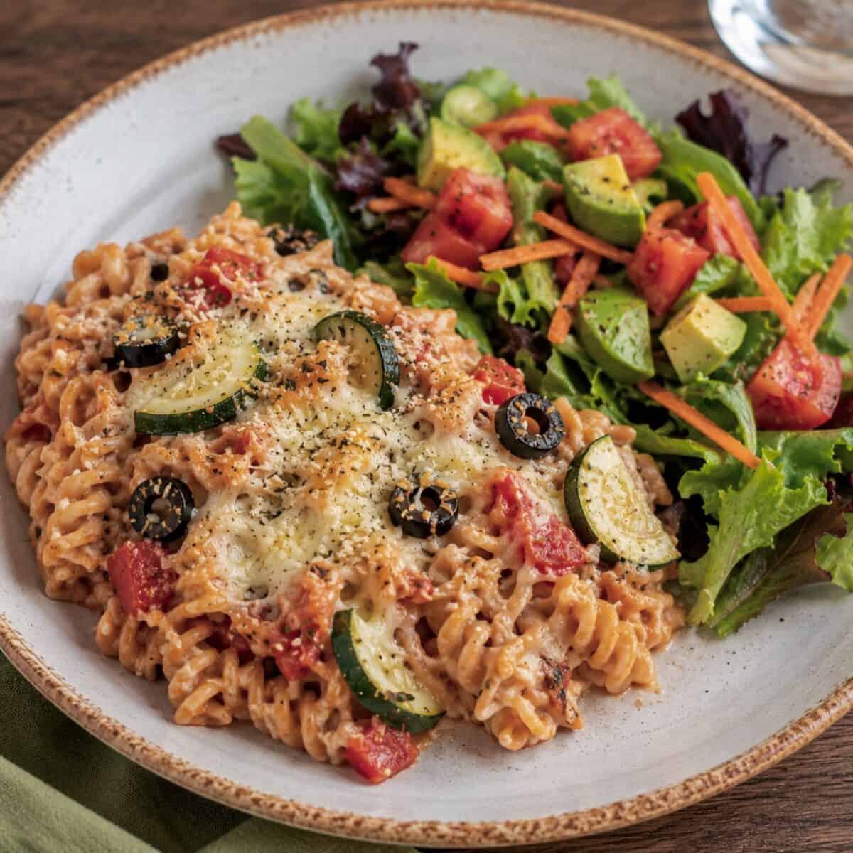 Baked pasta with cottage cheese and zucchini on a dinner plate with a mixed green salad.