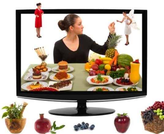 Television monitor with woman in front of table full of food with angel on one shoulder and devil in red dress on other shoulder.