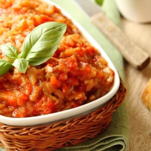 Roasted Eggplant Spread with basil garnish in a white dish in a basket on a table with a piece of bread