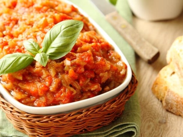 Roasted Eggplant Spread with basil garnish in a white dish in a basket on a table with a piece of bread